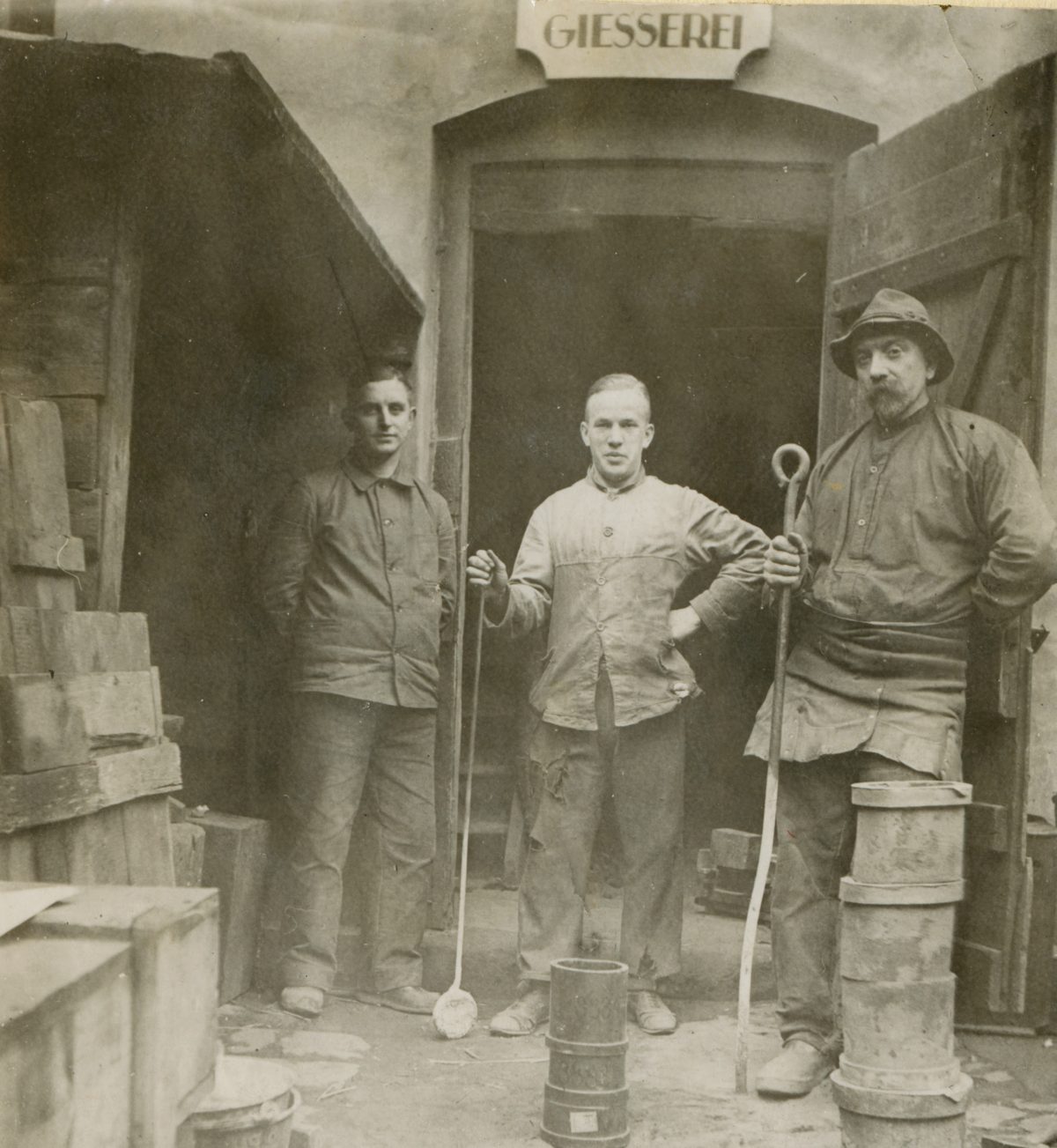 Arthur Symanzik, Anton Schuck und Georg Knoche in Arbeitskleidung vor dem Tor der Gießerei, historische Aufnahme