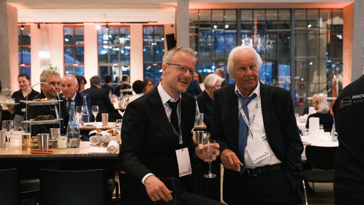Sandor Winter und Dieter Winter im Anzug bei der Jubiläumsfeier, im Hintergrund festlich gedeckte Tische