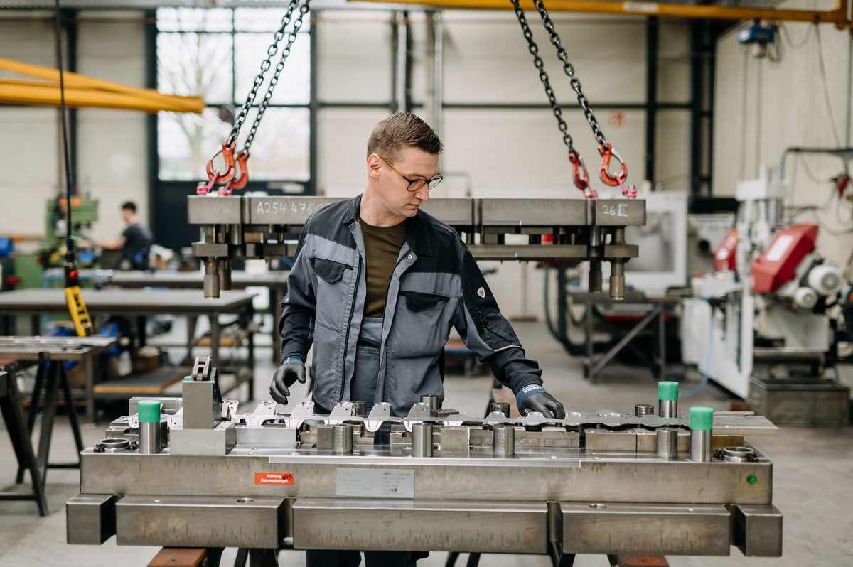 Werkzeugmechaniker prüft ein am Kran hängendes Werkzeugoberteil